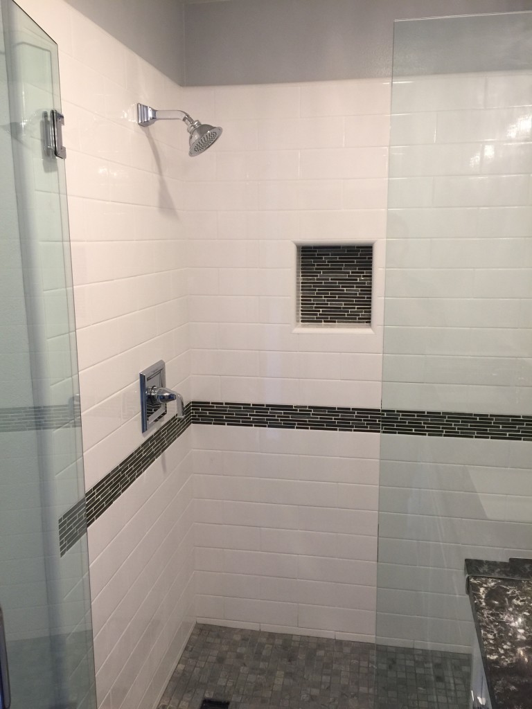 white subway tile with contrasting black tile at chair rail level with black glass tile in the shower niche