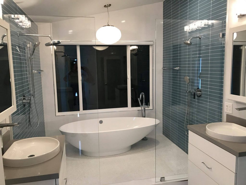 Orange County bathroom remodel company creates a wet room with two shower heads and a white tube enclosed by glass