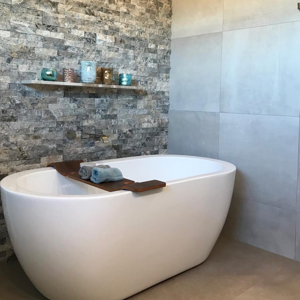local home remodeling contractor after picture of white tub with a stacked stone wall and wood shelf