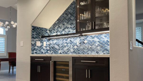 Home bar with custom blue glass backsplash in wave pattern and dark wood custom cabinets