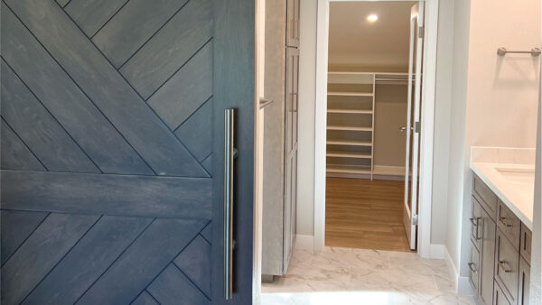 Master bathroom retreat with wood-tone barn door, marble look tile, and custom closet design