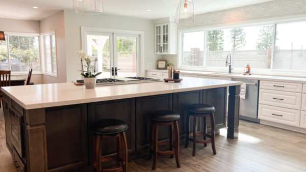 Open concept kitchen with wood tone island with seating and white perimeter cabinets with lighter wood tone porcelain tile floors