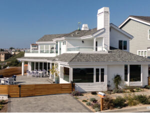 Exterior of home in Dana Point with white siding, large windows, mahogany wood fence and gray-tone pavers