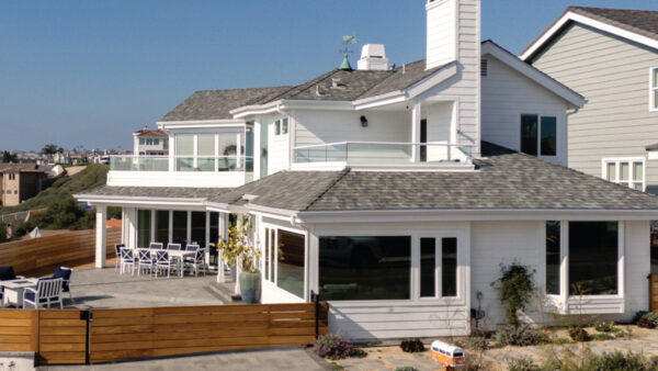 Exterior of home in Dana Point with white siding, large windows, mahogany wood fence and gray-tone pavers