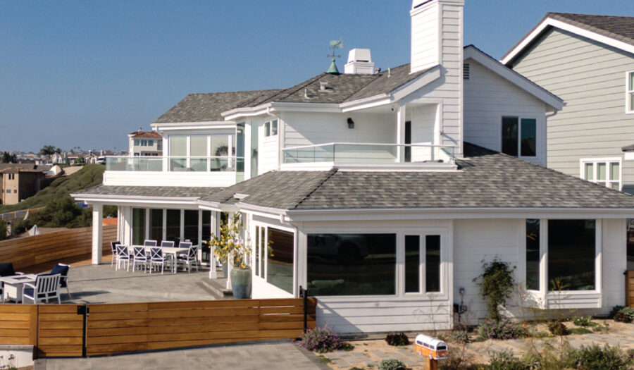 Exterior of home in Dana Point with white siding, large windows, mahogany wood fence and gray-tone pavers