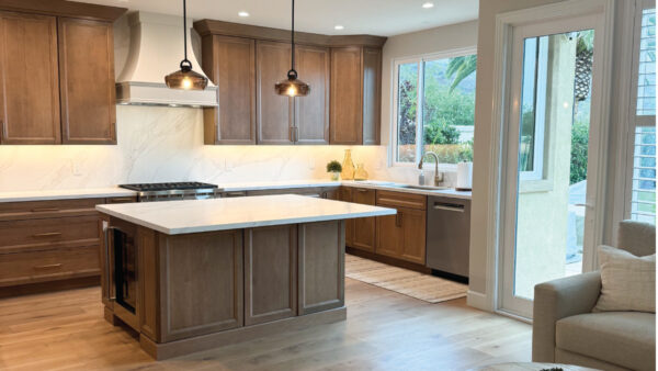 Wood tone kitchen cabinets with statement white hood and quartz countertops, with a lighter tone engineered hardwood floor.