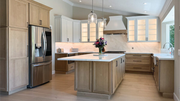 Kitchen design with medium toned lower cabinets and island and warm white uppers with custom hood and pendant lighting